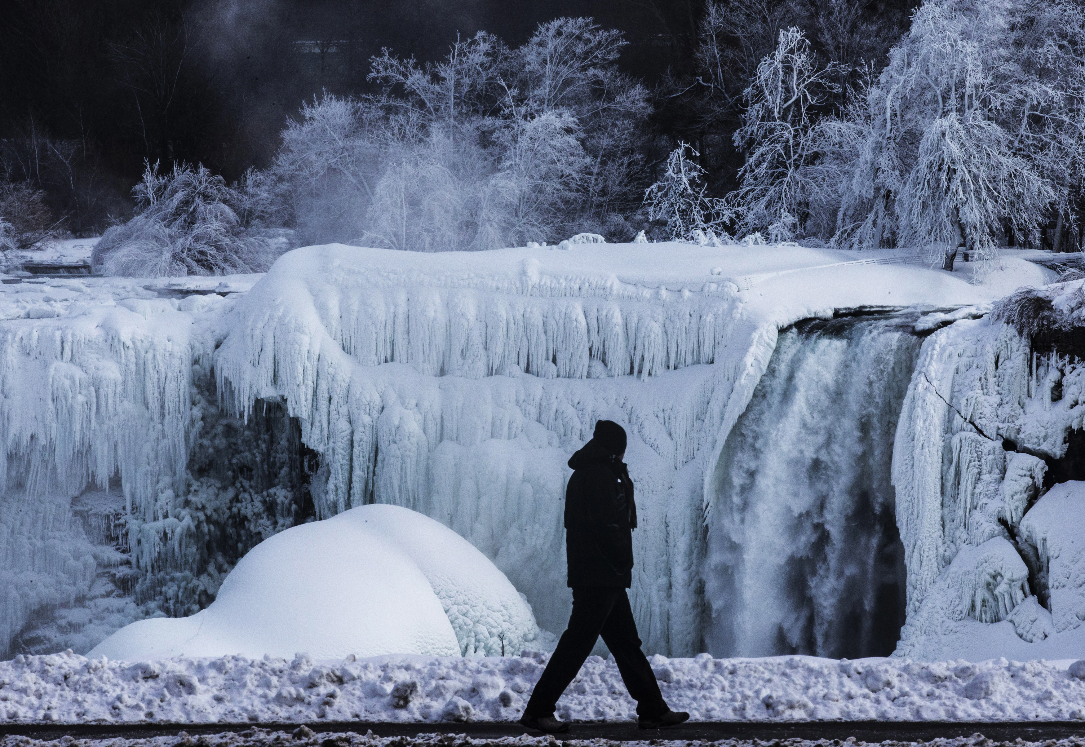 A man walks in front of partially frozen American side of Niagara Falls on during sub-freezing temperatures in Niagara Falls